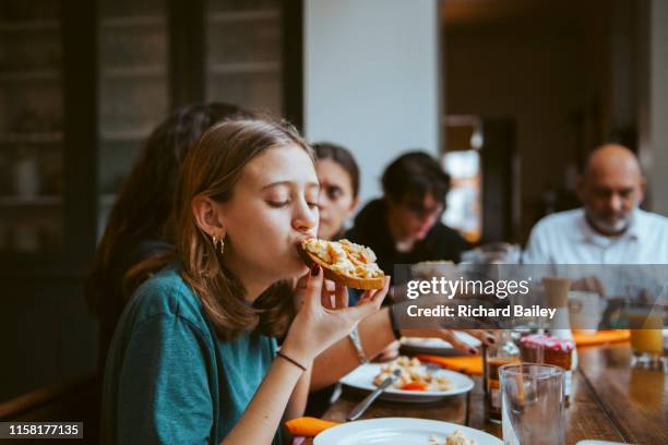 teenage girl eating a scrambled egg sandwich at breakfast - family teenager home life stock-fotos und bilder