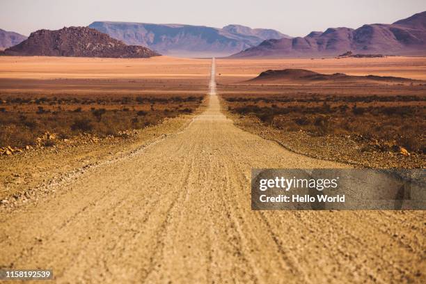 beautiful empty dirt road in desert plain with mountains in background - schotterstrecke stock-fotos und bilder