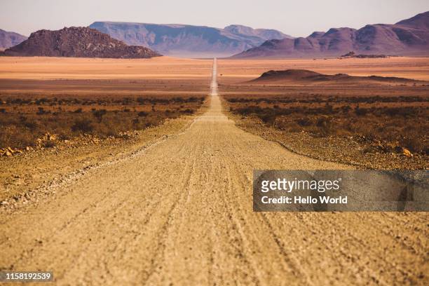 beautiful empty dirt road in desert plain with mountains in background - encoger fotografías e imágenes de stock