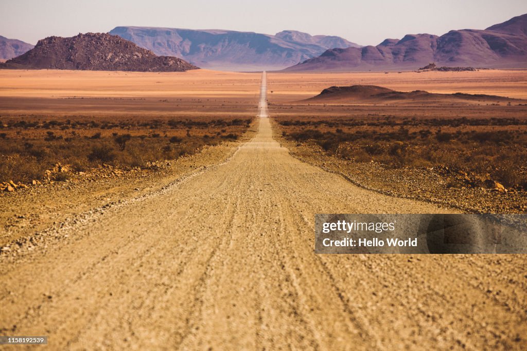 Beautiful empty dirt road in desert plain with mountains in background