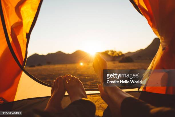 view from inside tent of feet and sun setting - orange colour stock-fotos und bilder