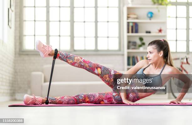 joven mujer deportiva atractiva practicando ejercicio con banda de resistencia en casa - goma elástica fotografías e imágenes de stock
