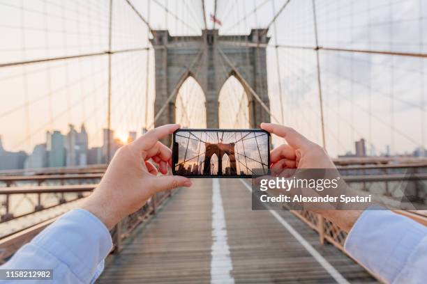 personal perspective view of a man photographing brooklyn bridge using smartphone, new york, usa - fotoberichten stockfoto's en -beelden