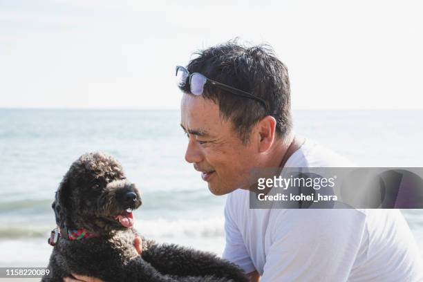 aziatische man met hond ontspannen in het strand - middle age man and walking the dog stockfoto's en -beelden