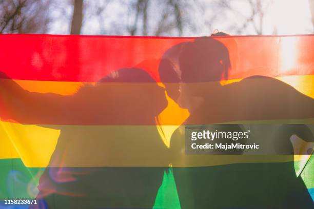 menschen, homosexualität, gleichgeschlechtliche ehe, schwulen- und liebeskonzept - nahaufnahme des glücklichen lesbischen paares, das die hände über regenbogenflagge hält - ehe gleichberechtigung stock-fotos und bilder