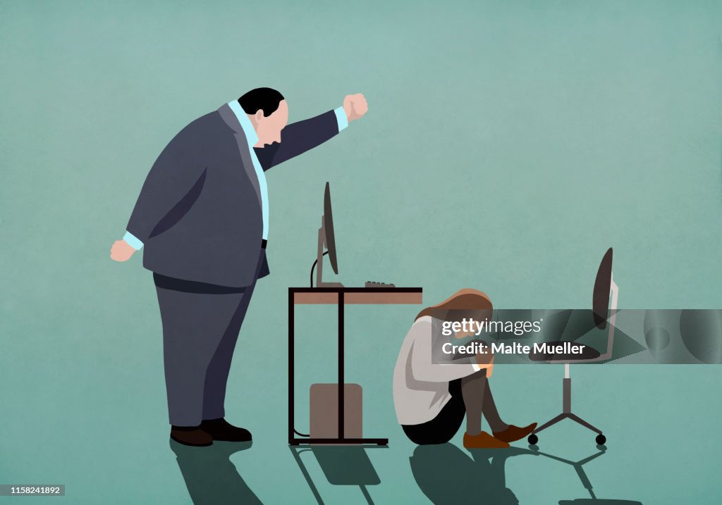 Angry businessman threatening businesswoman crouched under desk