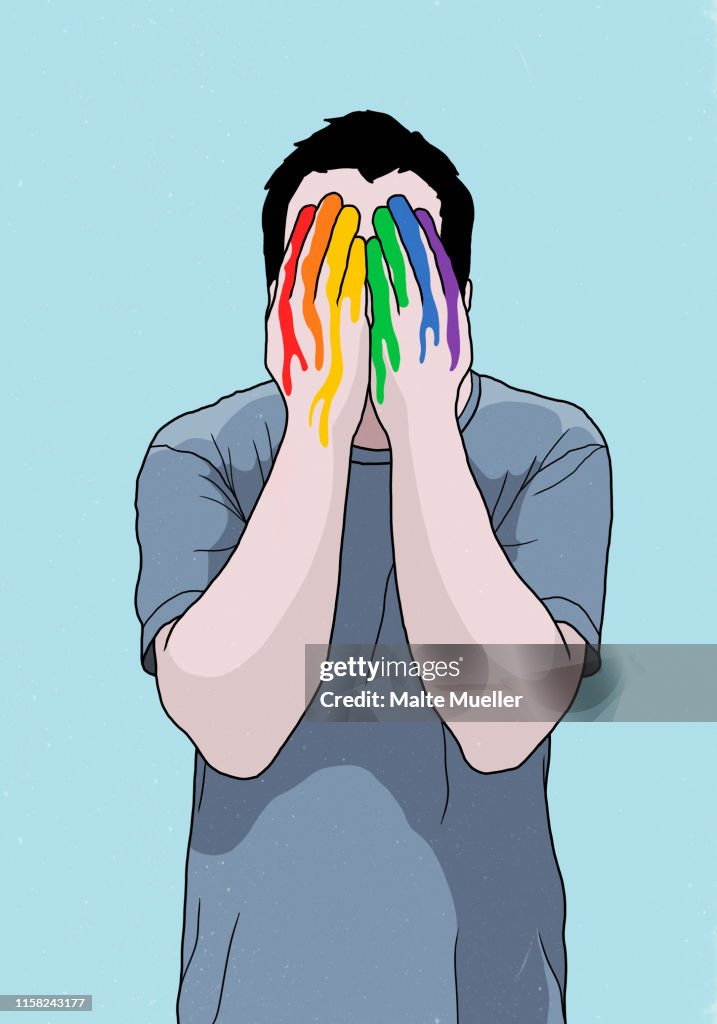 Man covering face with rainbow painted hands