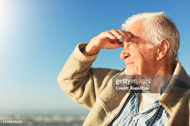 handsome senior man shields his eyes against bright sun by the sea - blocking sun stock pictures, royalty-free photos & images