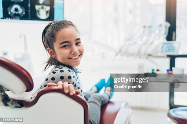 porträt eines lächelnden mädchens, das auf einem zahnarztstuhl sitzt - pediatric dentistry stock-fotos und bilder