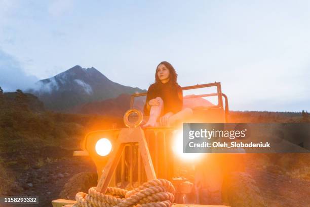 vista panorámica de la mujer sentada en el antiguo suv en el fondo del volcán merapi - vehicle light fotografías e imágenes de stock