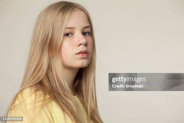 studio portret van een blonde tiener meisje in een geel t-shirt op een beige achtergrond - girl side view stockfoto's en -beelden
