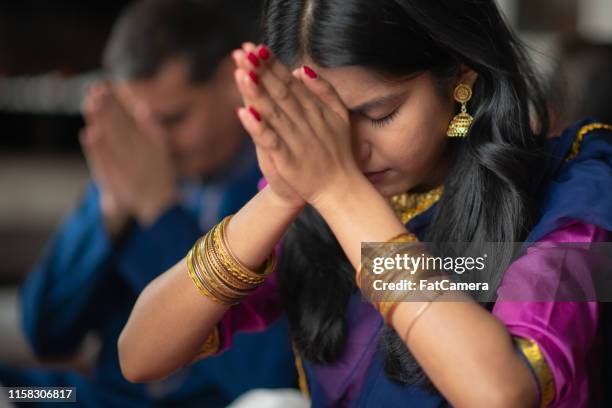 una hermosa familia india se sienta en su sala de estar una tarde rezando juntos. están celebrando y dando gracias durante las vacaciones diwali. se están uniendo a medida que se les baña con ropa tradicional. - hinduism fotografías e imágenes de stock