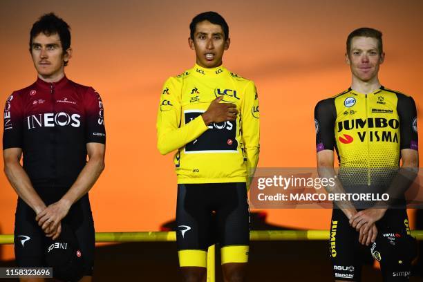 Colombia's Egan Bernal listens to his national anthem after receiving his overall leader's yellow jersey as he poses with second-placed Great...