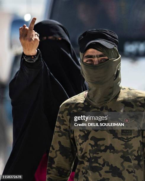 An internal security patrol member escorts a woman giving a middle-finger gesture, reportedly a wife of an Islamic State group fighter, in the al-Hol...