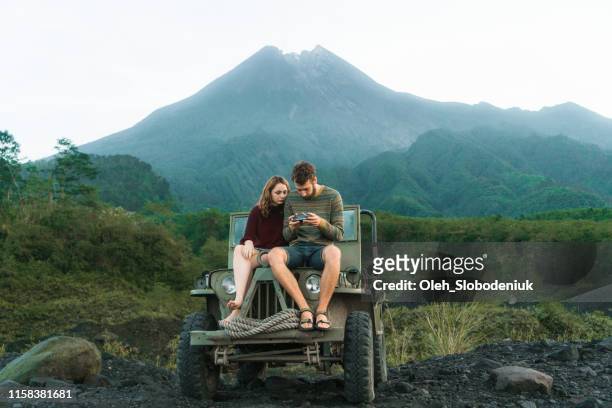 Scenic view of couple sitting on old fashioned SUV on the background of Merapi volcano