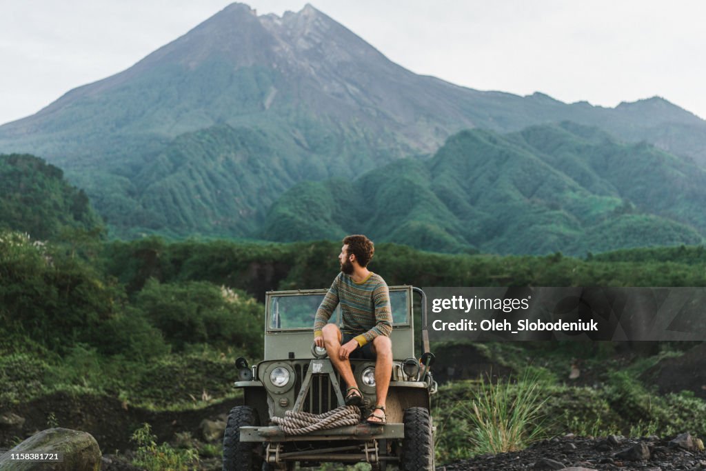 Mann sitzt auf altmodischem SUV im Hintergrund des Vulkans Merapi