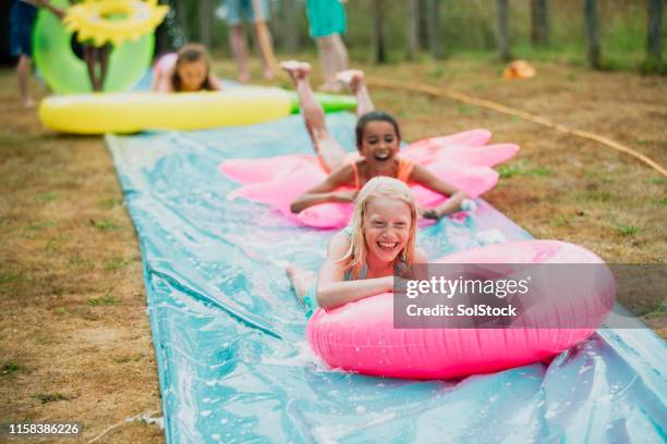 children having fun on a slip 'n' slide - backyard water slide stock pictures, royalty-free photos & images