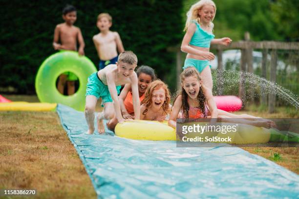 playing on the slip 'n' slide with friends - backyard water slide stock pictures, royalty-free photos & images