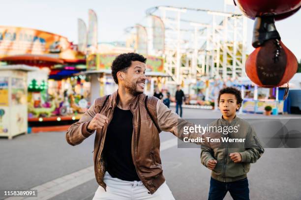 father about to hit punching bag at fun fair - fair game foto e immagini stock