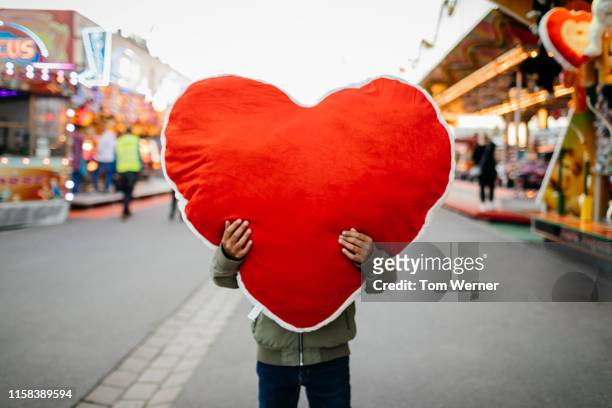 young boy holding large soft heart toy at fun fair - an evening with heart fotografías e imágenes de stock