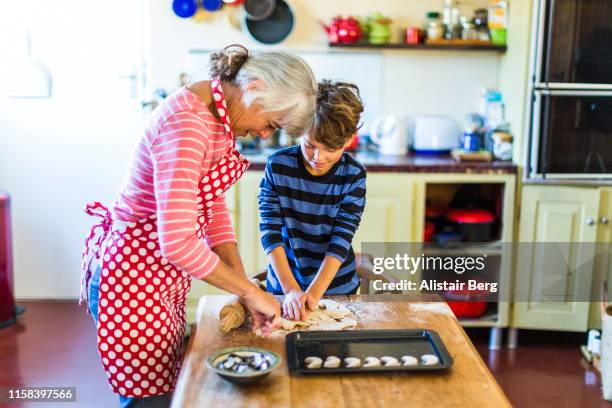 grandmother helping her grandson to bake biscuits in kitchen - making cookies stock pictures, royalty-free photos & images