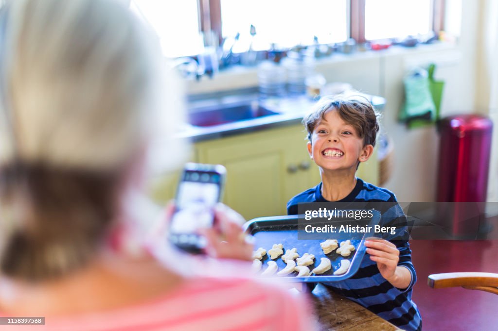 Grandmother photographing her grandson in kitchen with phone