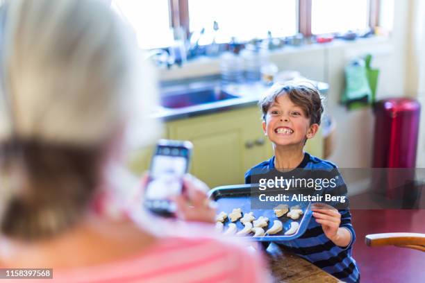 Grandmother photographing her grandson in kitchen with phone