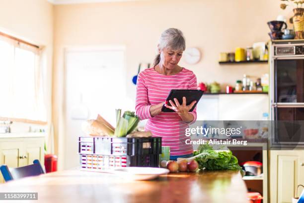 senior woman checking her fresh vegetable delivery - senior women shopping stock pictures, royalty-free photos & images