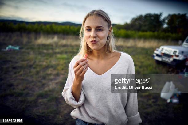 portrait of young woman eating a carrot in the countryside - capelli biondi foto e immagini stock