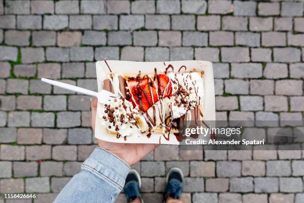 eating belgian waffle with sweet toppings and fresh fruits at the town square, personal perspective view - brüssel stock-fotos und bilder