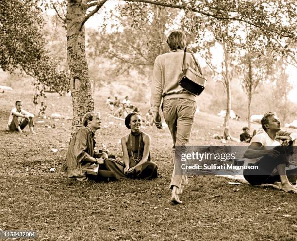 Tall, blond, barefooted man with a camera bag heading home, as a happy couple observe, several barefooted young men sitting on the grass at the 1st...