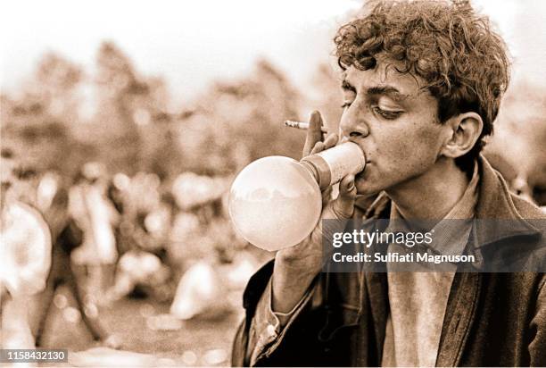 Curly-haired young man inhaling nitrous oxide, with a cigarette in his hand at the 1st Elysian Park Love-In on March 26, 1967 in Los Angeles,...