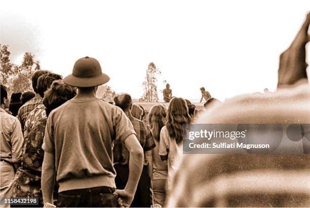Backs of the crowd watching bare-chested men sitting on the top of the historic train car, one man in a pith helmet at the 1st Elysian Park Love-In...