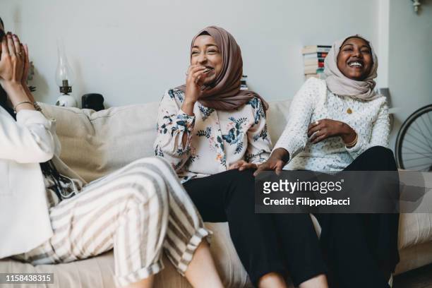three friends talking together sitting on the sofa at home - islam stock pictures, royalty-free photos & images