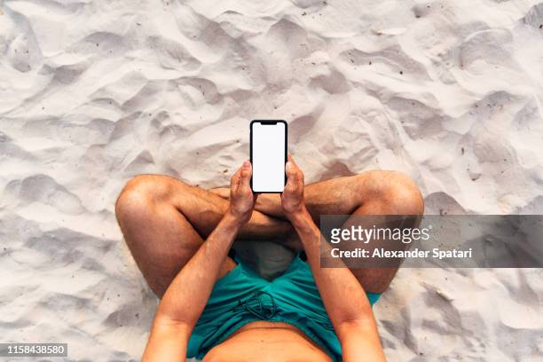 man using smartphone at the beach, personal perspective directly above view - smartphone strand stock-fotos und bilder