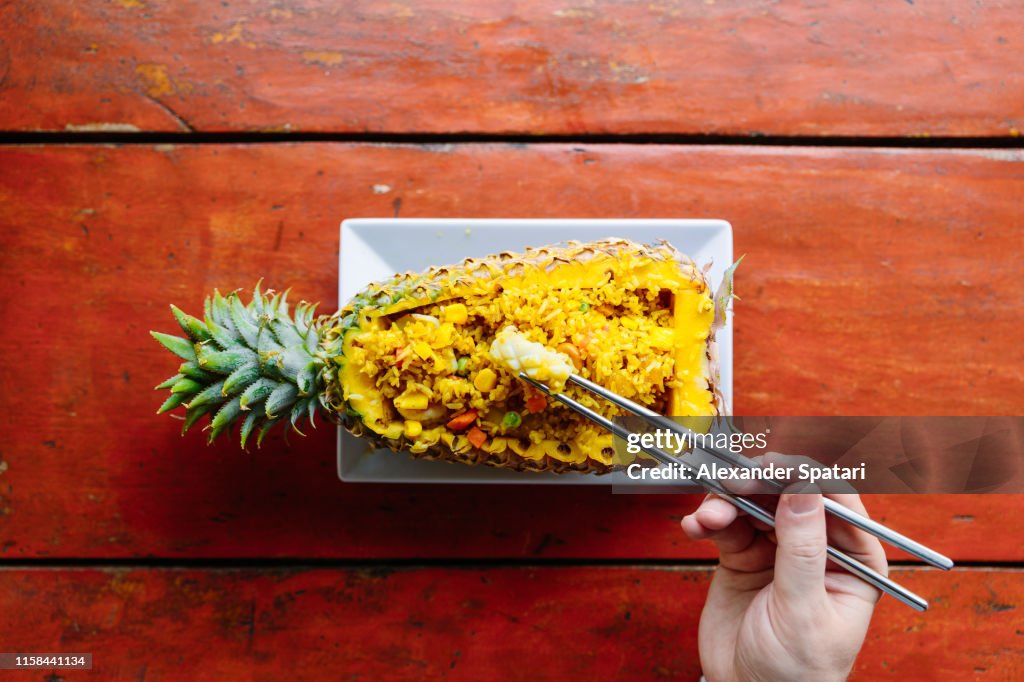Man eating rice with chopsticks from a pineapple, directly above view
