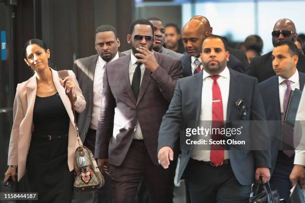 Singer R. Kelly covers his mouth as he speaks to members of his entourage as he arrives at the Leighton Criminal Courts Building for a hearing on...