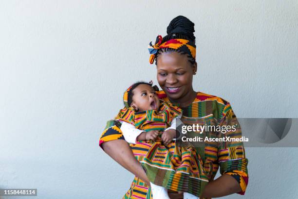 lächelnde mutter trägt süße tochter gegen wand - afrikanische kultur stock-fotos und bilder