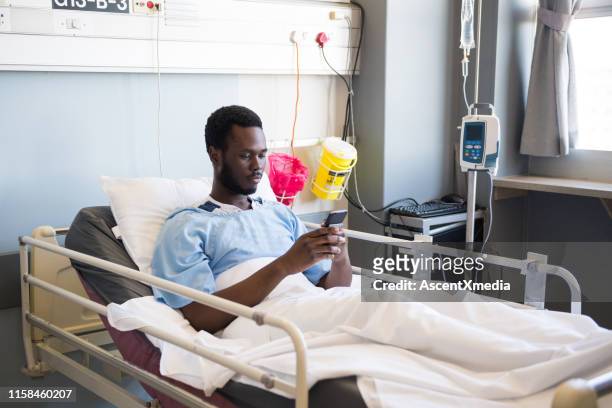 männlicher patient mit smartphone, während er auf dem bett liegt - adult male hospital bed stock-fotos und bilder