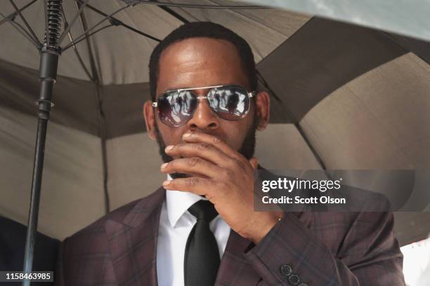 Singer R. Kelly covers his mouth as he speaks to members of his entourage as he leaves the Leighton Criminal Courts Building following a hearing on...