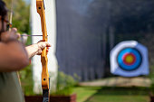 Archer holding wooden bow and aiming at unfocused target board