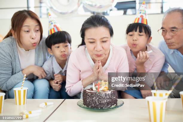 grandmother blowing birthday candles - parents children blow candles asians stock pictures, royalty-free photos & images