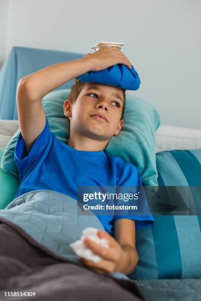 zieke jongen in bed met ijs zak op zijn hoofd - ijszak stockfoto's en -beelden