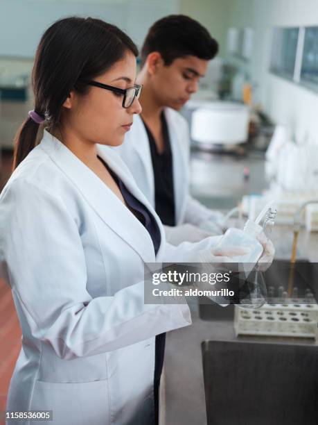 female student wearing gloves and pouring liquid in flask - scientific flask stock pictures, royalty-free photos & images