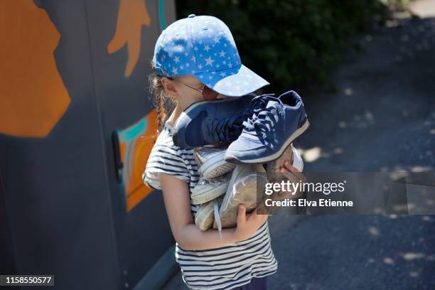child (6-7) carrying pile of old shoes for recycling at a recycling centre - declutter stockfoto's en -beelden