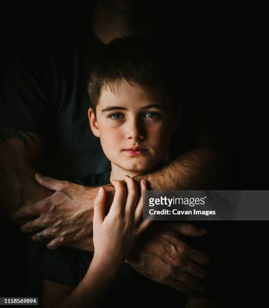 close up portrait of a boy with his father's arms wrapped around him. - human arm stock pictures, royalty-free photos & images
