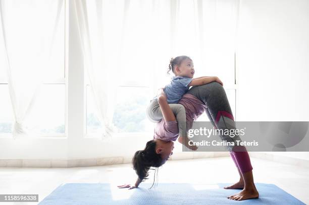 woman doing yoga with daughter on her back - atlete stockfoto's en -beelden