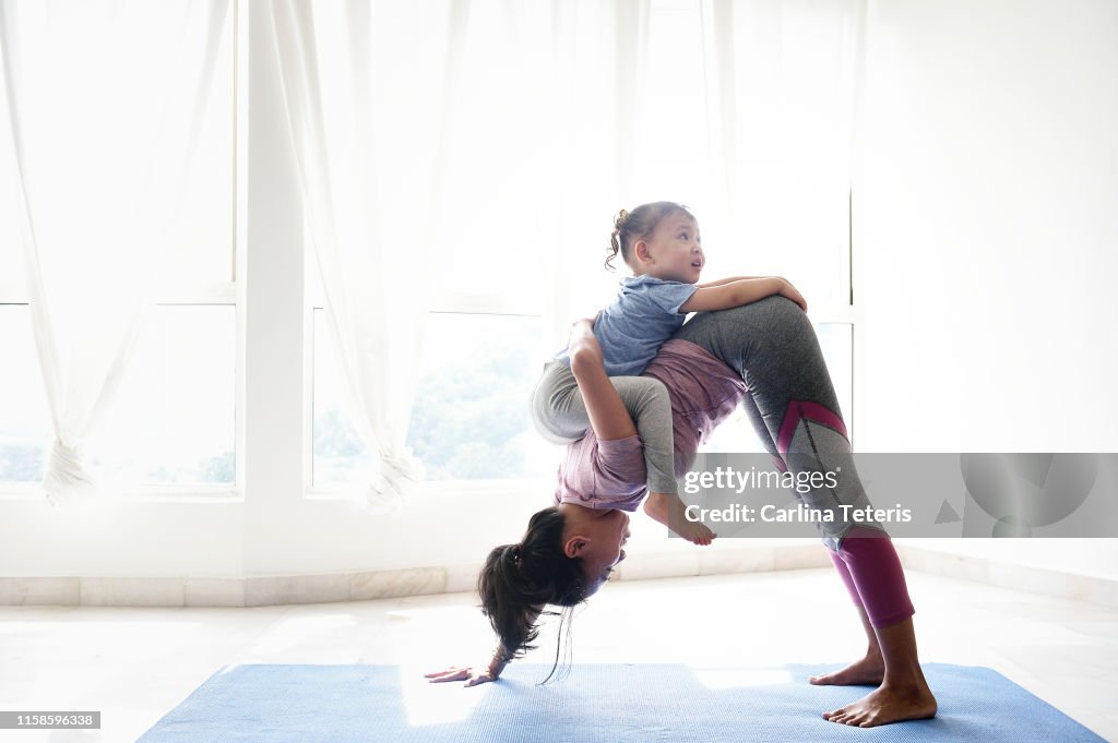 Woman doing yoga with daughter on her back