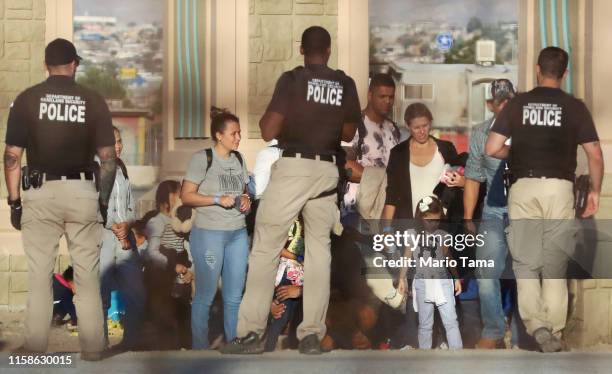 As seen through fencing, migrants stand while being detained by Department of Homeland Security police after crossing to the U.S. Side of the...