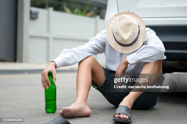 a drunken man driving a car with a bottle of alcohol in his hand.a man holds a driving wheel and a bottle of beer. - dronken stockfoto's en -beelden